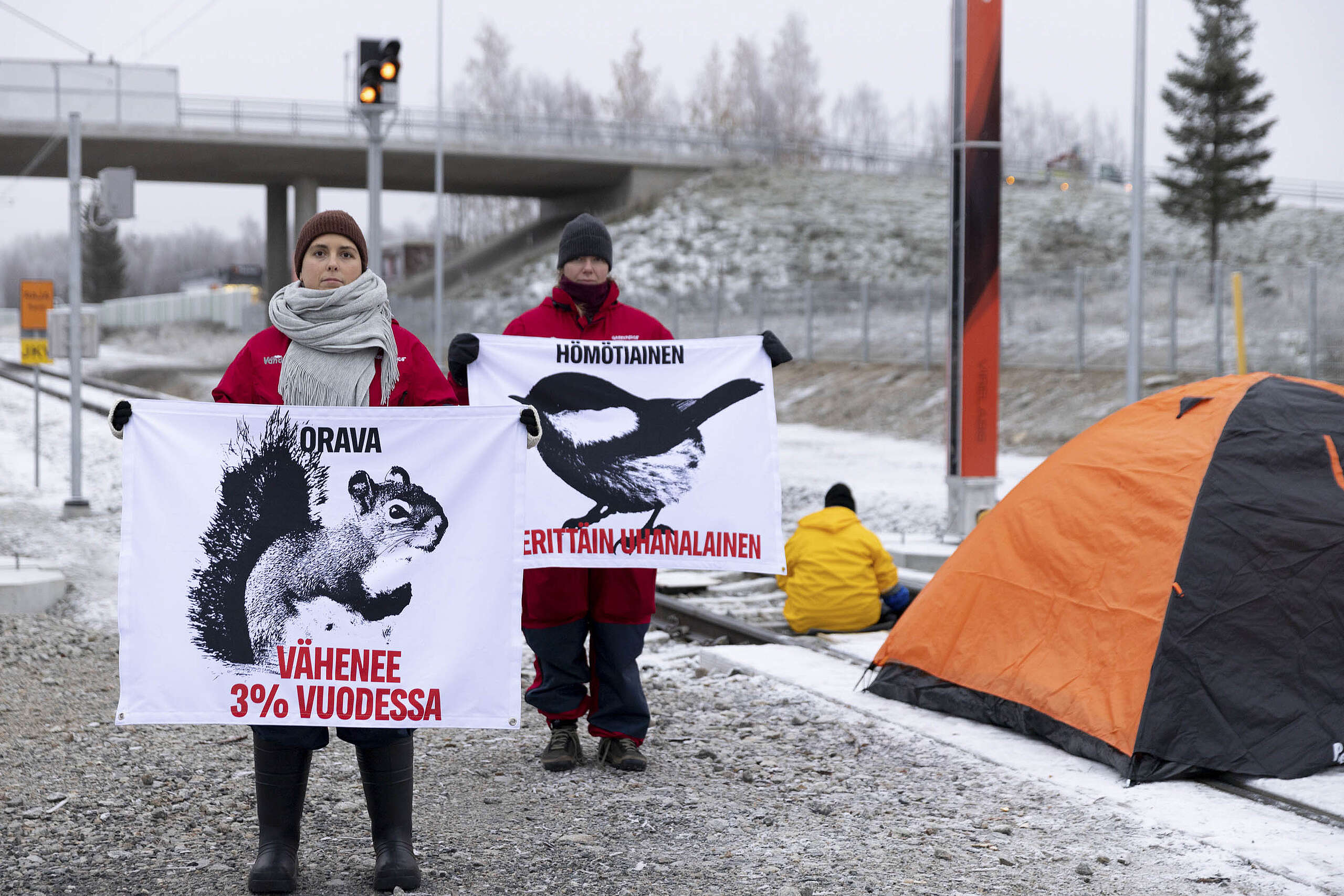 Junaraiteiden vieressä seisovat Greenpeacen työntekijät pitelevät bannereita, joissa muistutetaan Suomen luonnosta vähenevistä lajeista.